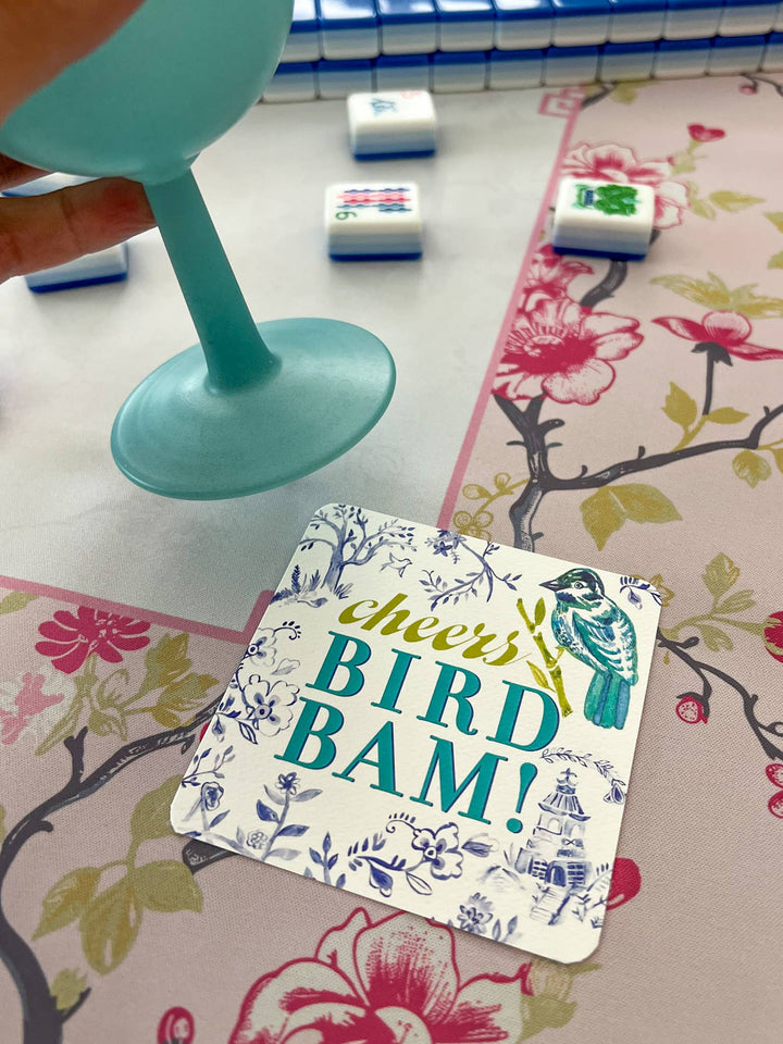 Coaster with 'cheers BIRD BAM!' text on a floral-patterned surface