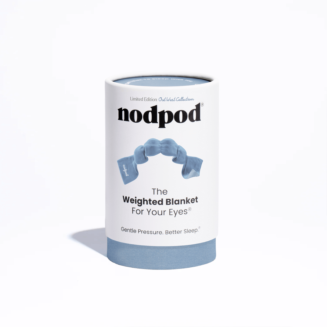 A cylindrical white product package for nodpod 'The Weighted Blanket For Your Eyes' with a light blue base and a blue graphic of a weighted blanket on the front, photographed on a clean white background.