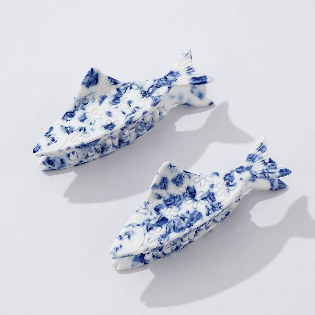 Two blue and white fish-shaped claw hair clips on a light gray background