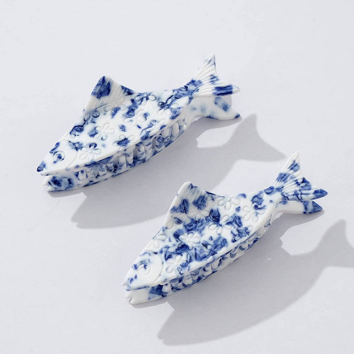 Two blue and white fish-shaped claw hair clips on a light gray background