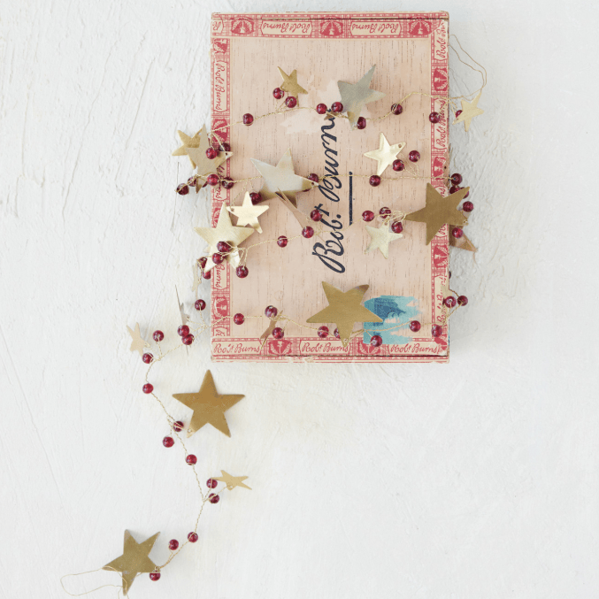 A vintage-style Christmas ornament box with a pink and gold patterned lid, decorated with gold star cutouts, red berry garlands, and a black script reading 'No. 14 Ornament'.
