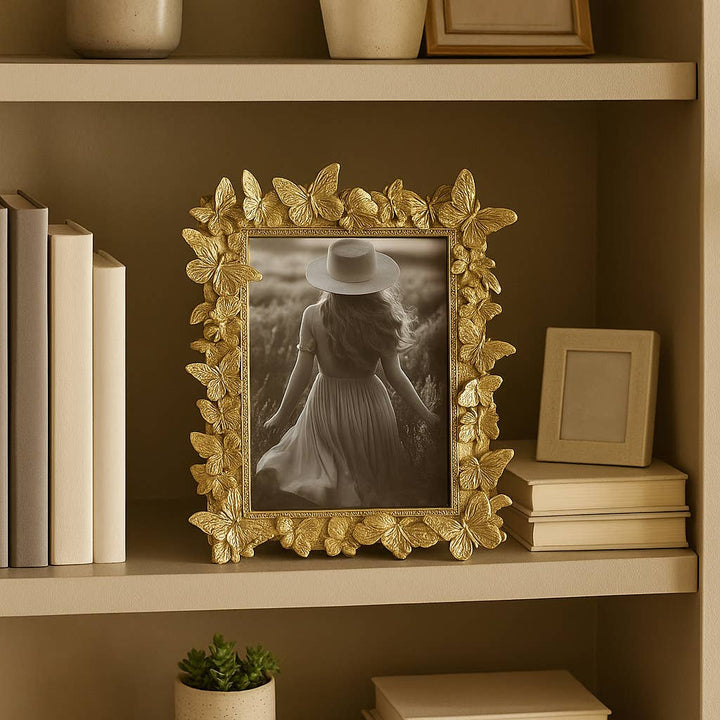 Decorative gold frame with a black and white photo of a person on a shelf with books and a plant.