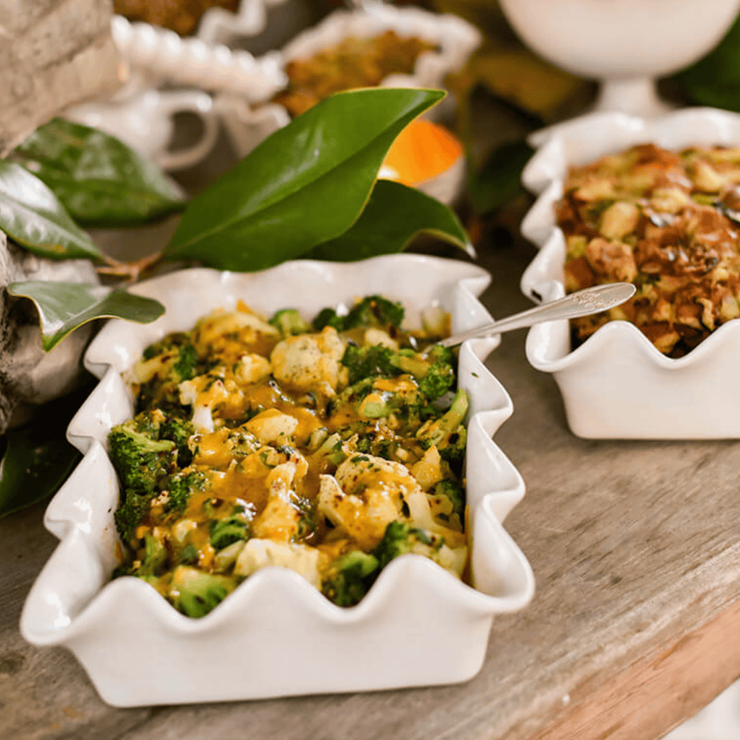 Two white ruffled dishes filled with a mixture of vegetables and grains on a wooden surface.