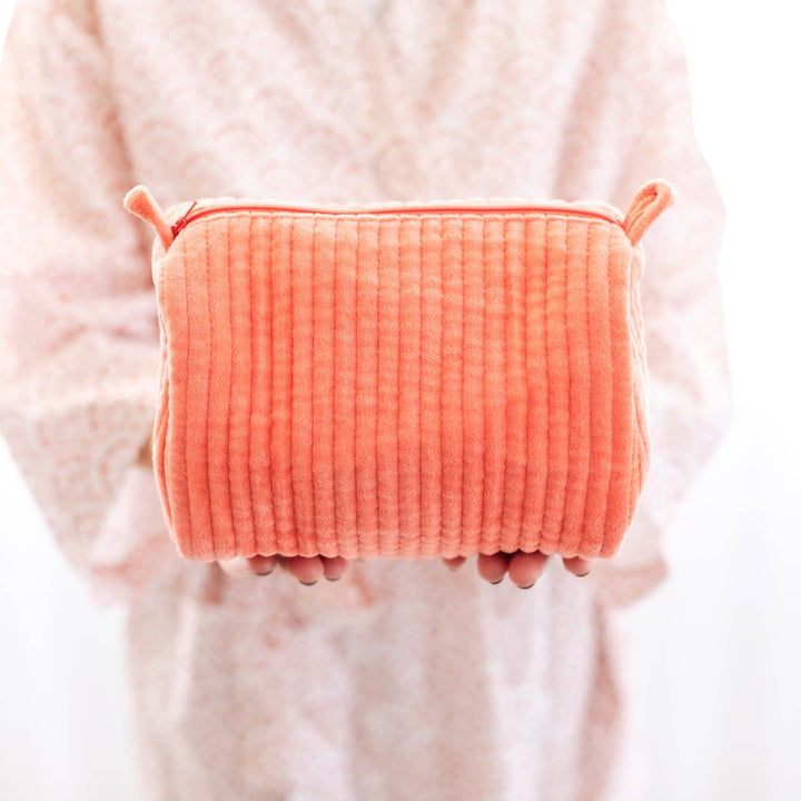 Person holding a textured orange pouch against a light background