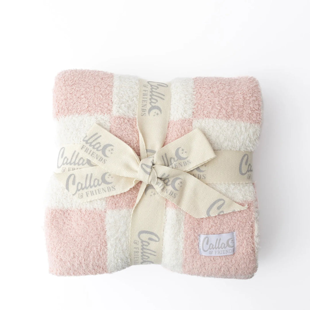 A folded plush checkered blanket in soft pink and cream, wrapped with a cream ribbon printed with the brand name 'Calla Friends' and tied in a bow, on a white background.
