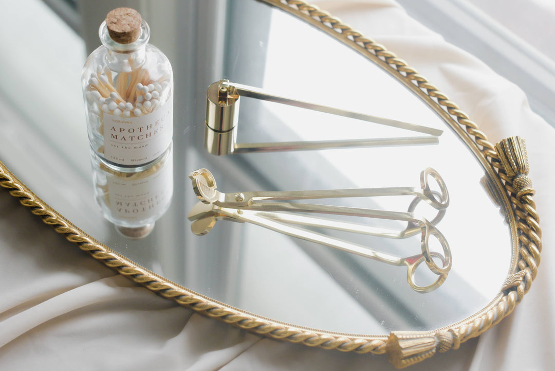 Candle snuffer and other candle accessories on a mirrored tray.
