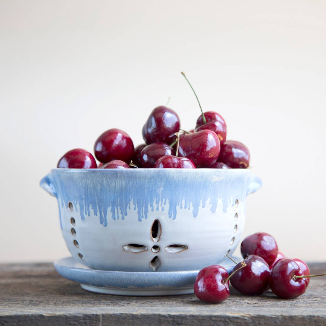 White colander filled with cherries on a wooden surface