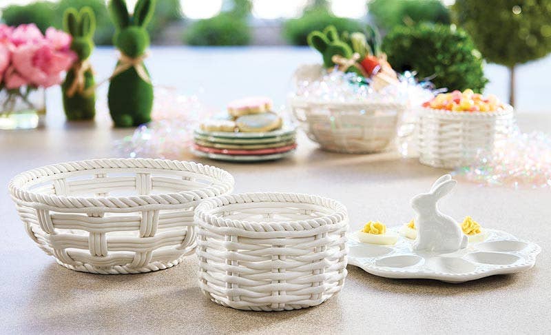 Two white woven basket-style bowls in different sizes on a tabletop, with Easter-themed decor and dishes blurred in the background.