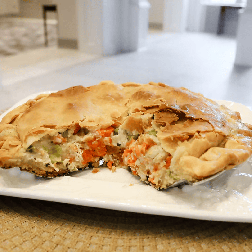 Vegetable pie on a white plate with a slice missing, placed on a woven mat.