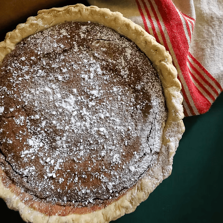 Chocolate pie with a lattice crust on a table with a rolling pin and towel.