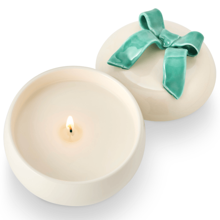 Round candle with a lit wick and a green ribbon on a white background