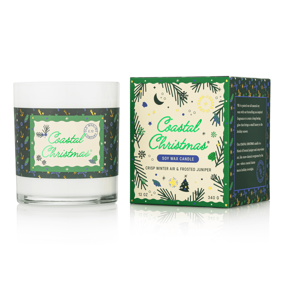 A Coastal Christmas soy wax candle in a clear glass jar with a white wax fill and a green patterned label, shown next to its matching green and cream retail box on a white background.