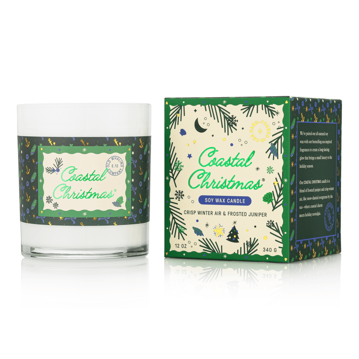 A Coastal Christmas soy wax candle in a clear glass jar with a white wax fill and a green patterned label, shown next to its matching green and cream retail box on a white background.