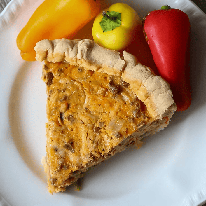 Slice of quiche on a white plate with colorful bell peppers