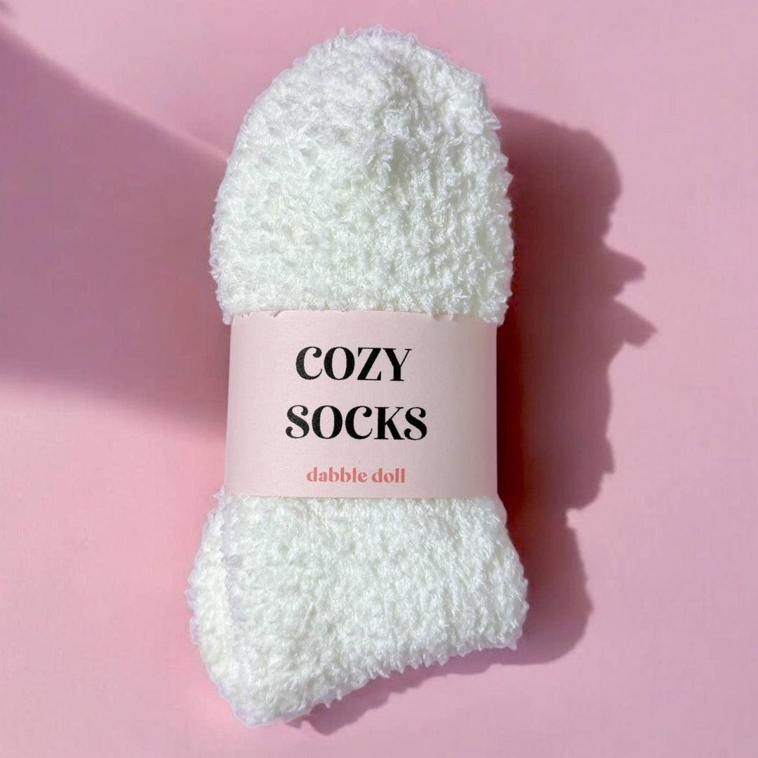 White fluffy sock with 'Cozy Socks' label on a pink background