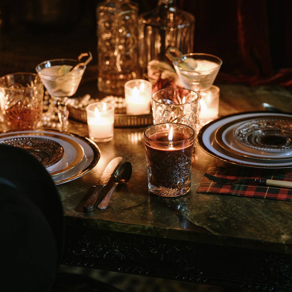 Dinner table setting with glasses, candles, and cutlery on a dark surface.