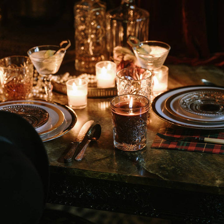 Dinner table setting with glasses, candles, and cutlery on a dark surface.