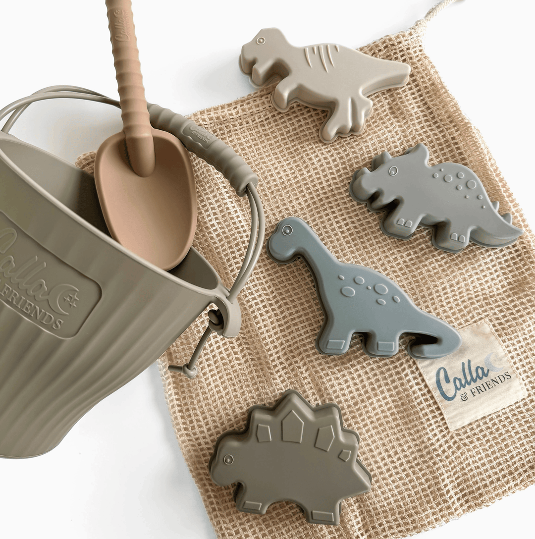 Children's playset with a sand pail, shovel, and dinosaur-shaped molds on a textured surface.