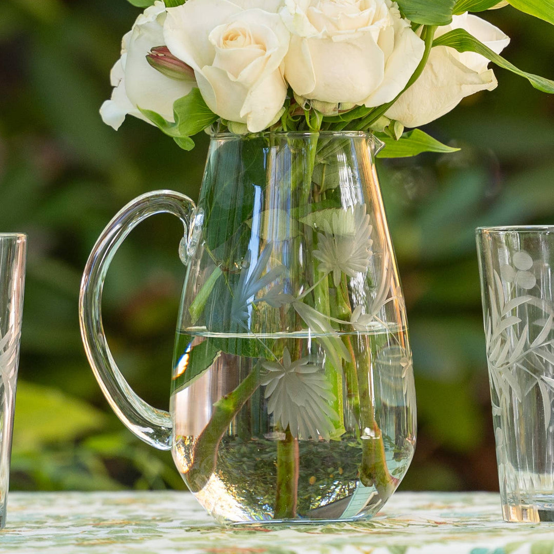 Clear glass pitcher with white flowers on a floral tablecloth