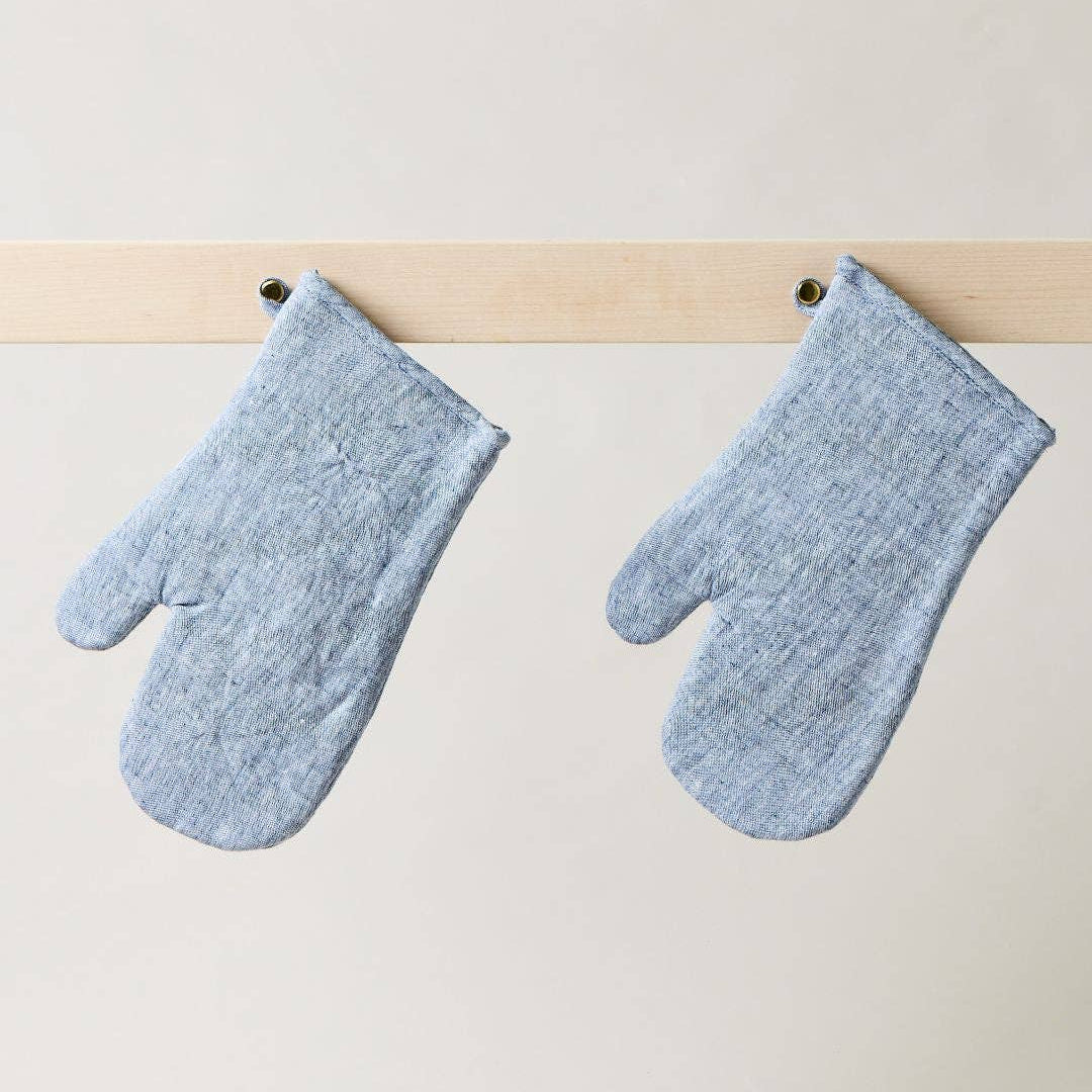 Pair of blue oven mitts hanging on a wooden rod against a white background