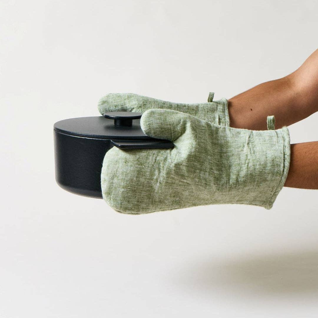 Person wearing a green oven mitt holding a black pot on a white background