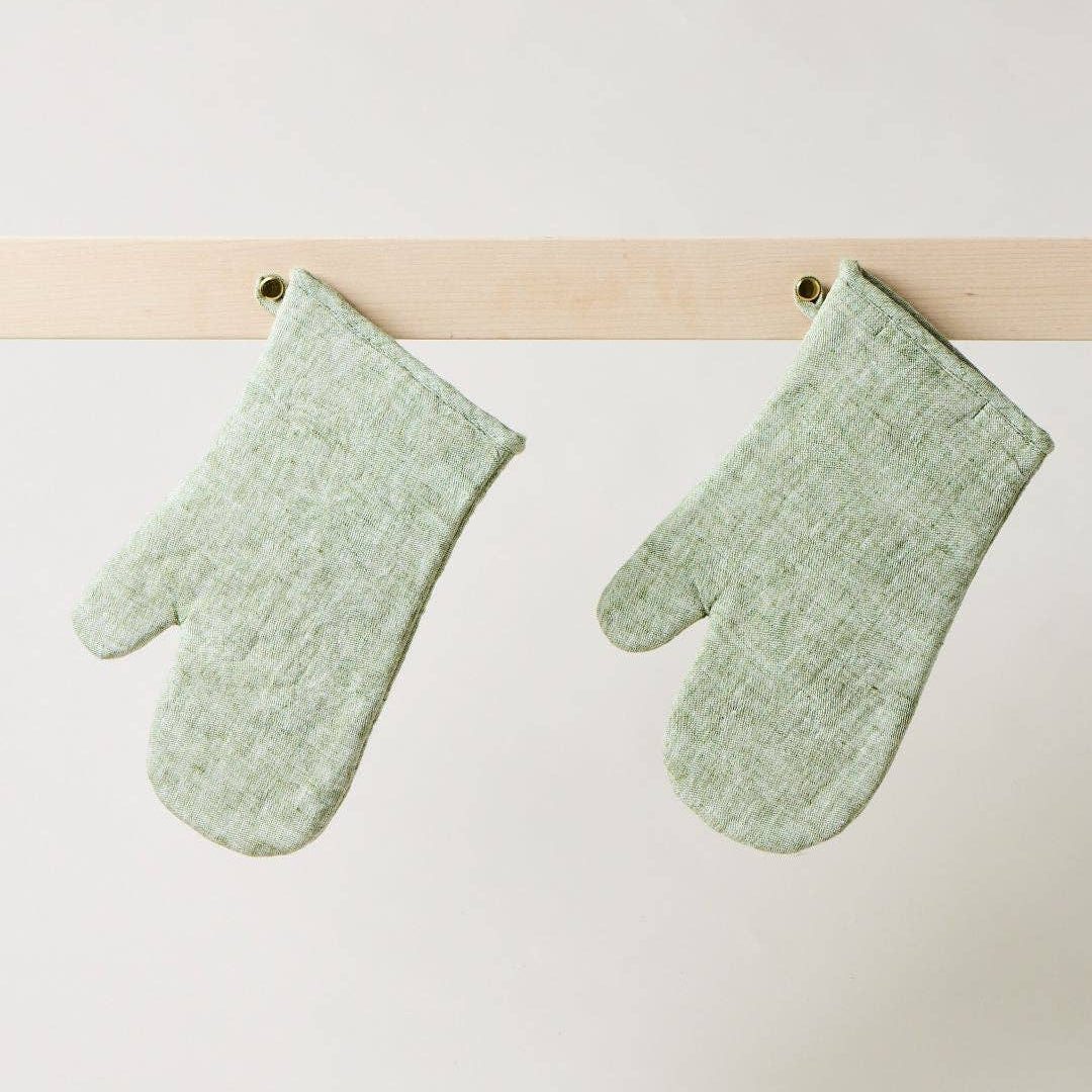Pair of green mittens hanging on a wooden rod against a white background