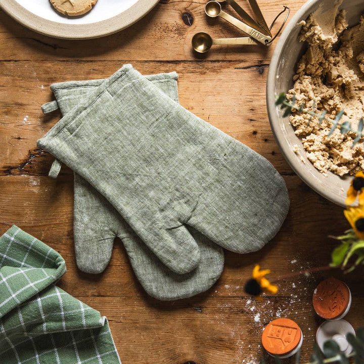 Green oven mitts on a wooden table with baking ingredients and tools.
