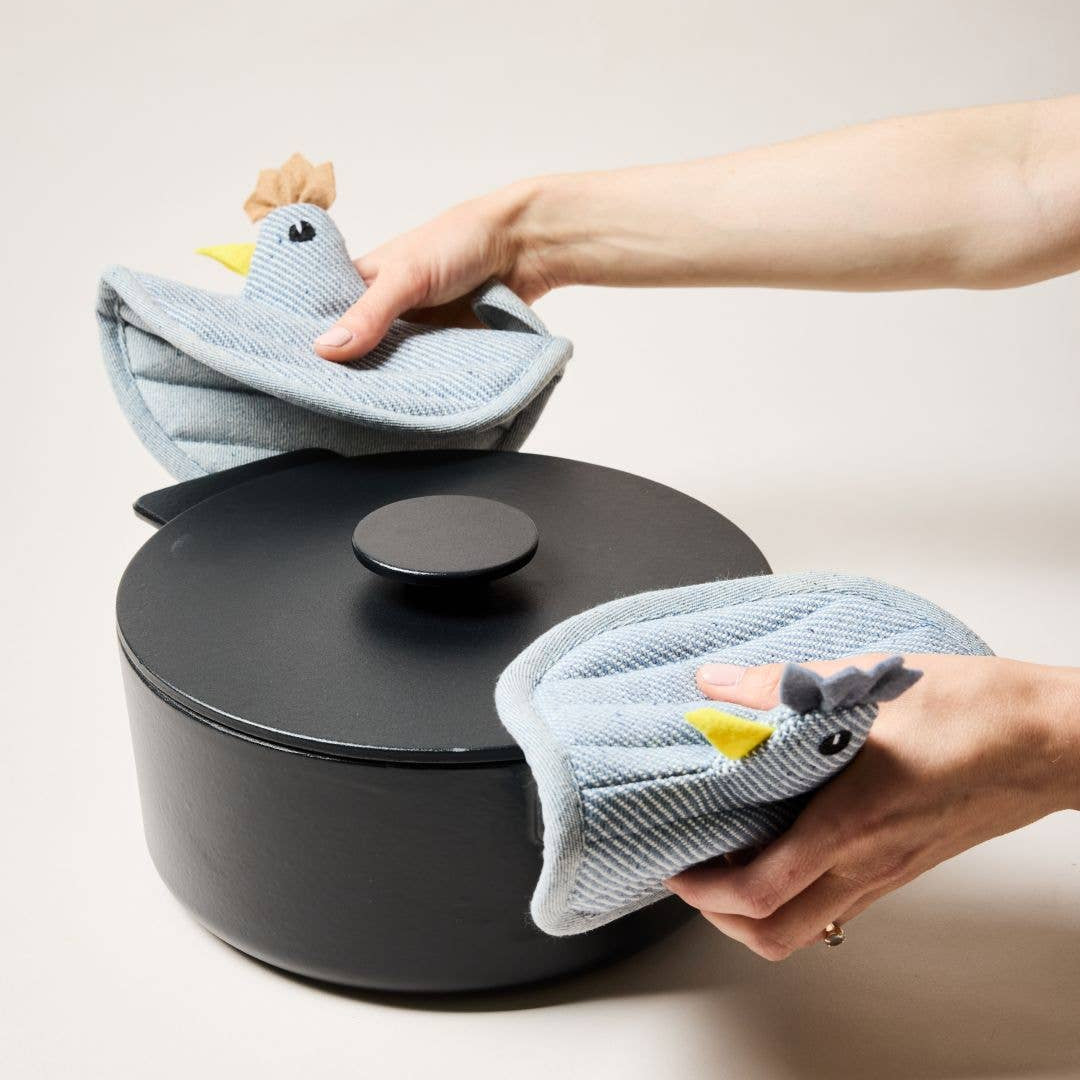 Person holding a hen potholders over a black pot on a light background