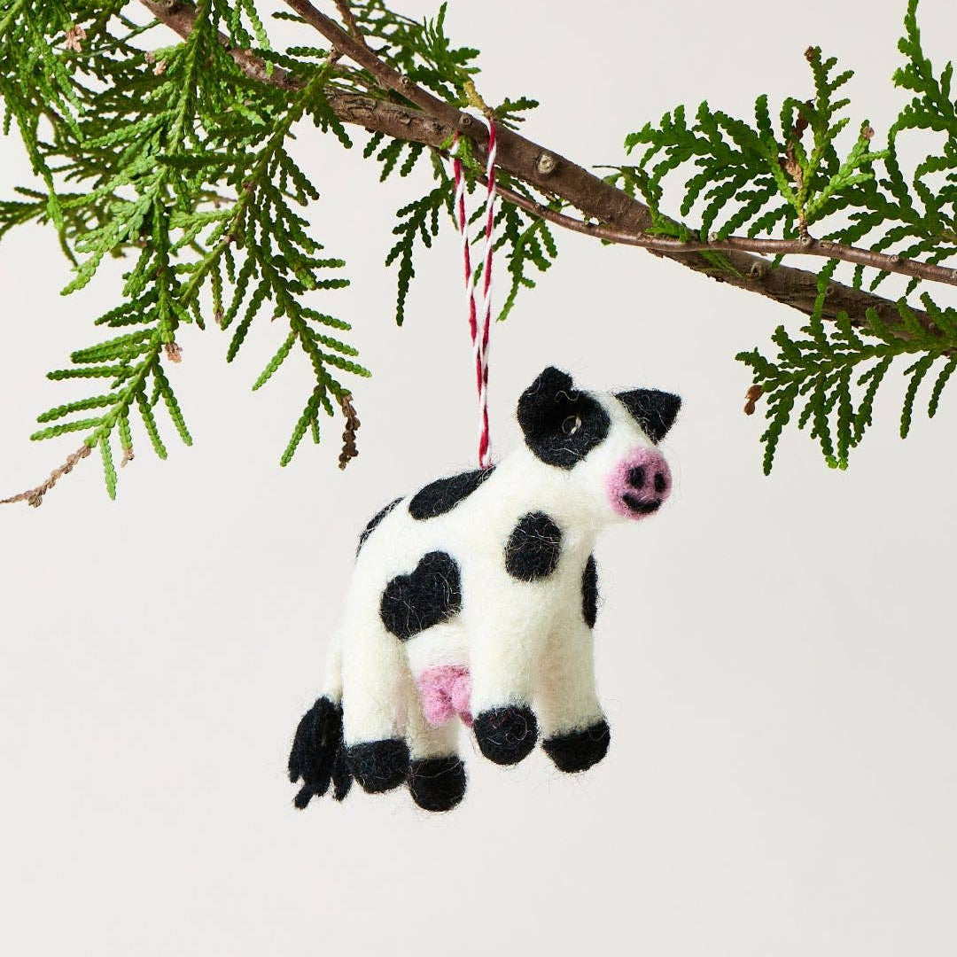 Cow-shaped ornament hanging from a branch on a light background