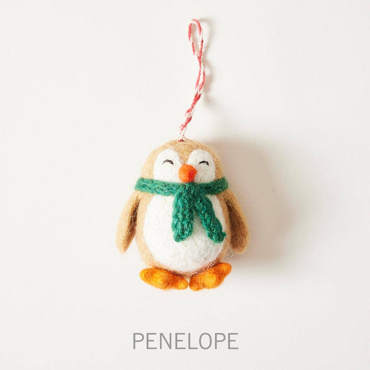Felted penguin ornament with a green scarf on a white background, branded 'Penelope'.