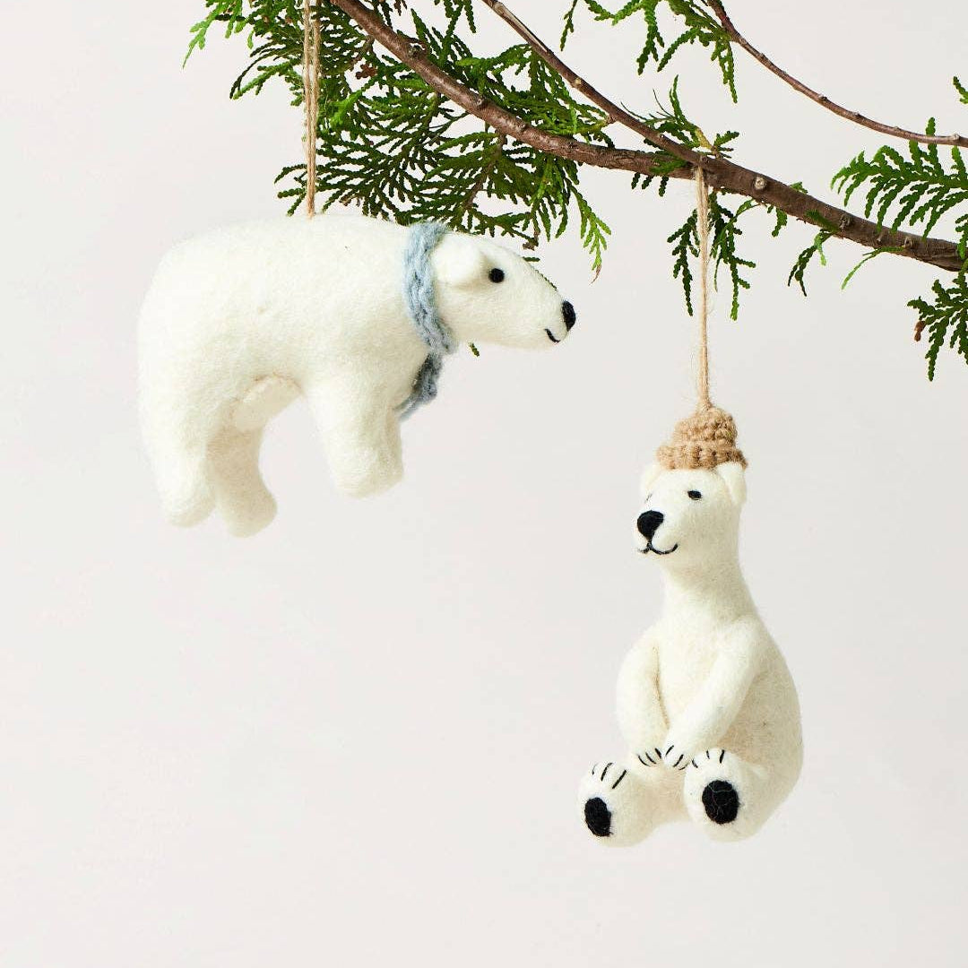 Two polar bear ornaments hanging from a tree branch against a light background