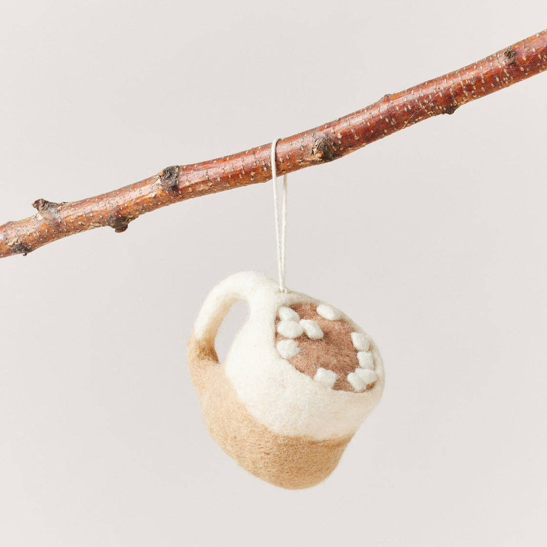 Decorative ornament shaped like a teacup with wooden handle hanging from a branch on a light background