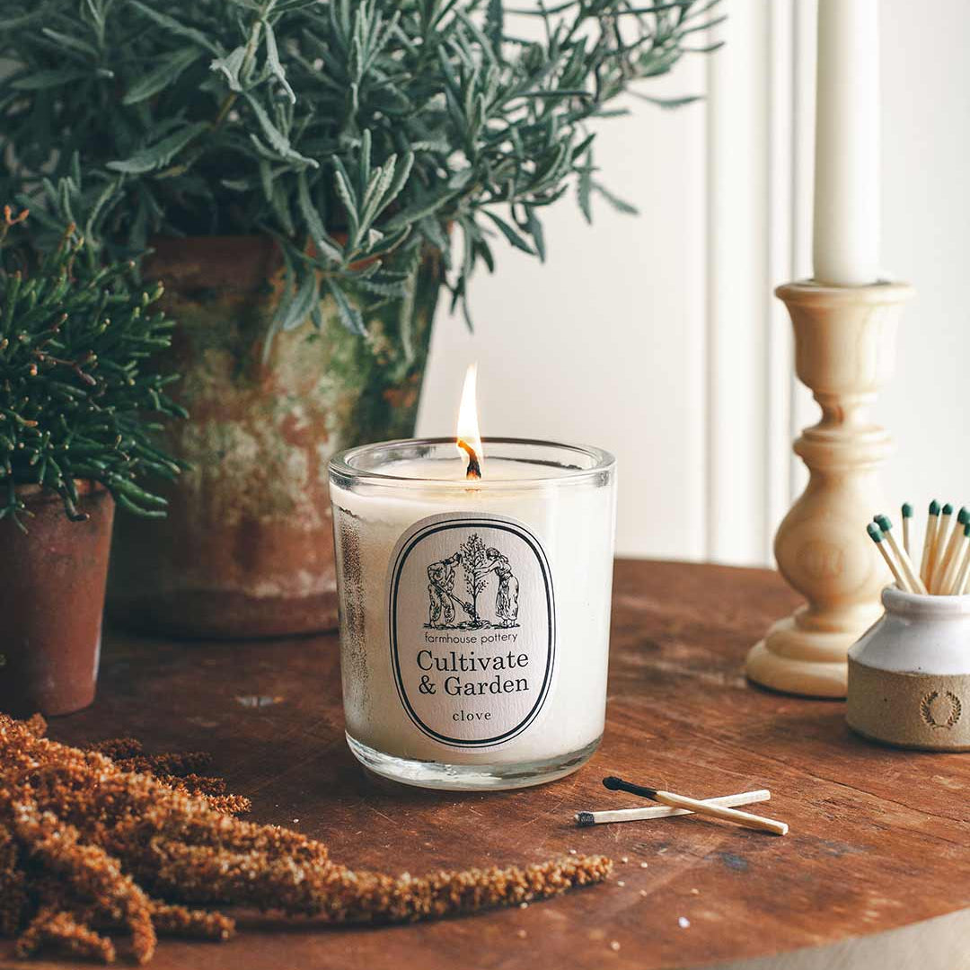 Candle with a label on a wooden table next to a plant and matches