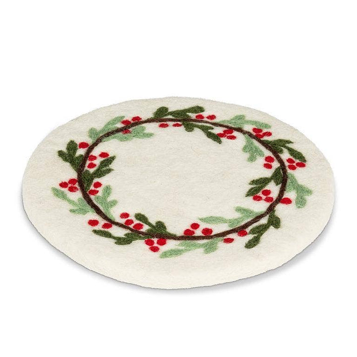 A round white felt trivetfeaturing a hand-picked holly wreath design with green leaves, red berries, and brown branches, set against a plain white background.