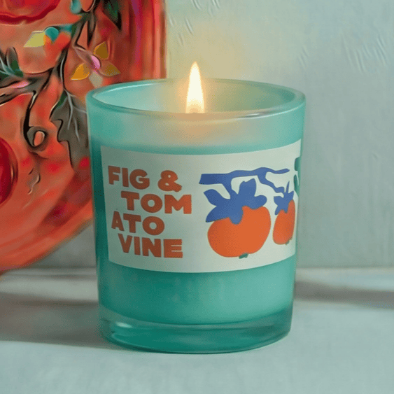 Candle with a label reading 'Fig & Tomato Vine' in front of a colorful decorative plate.