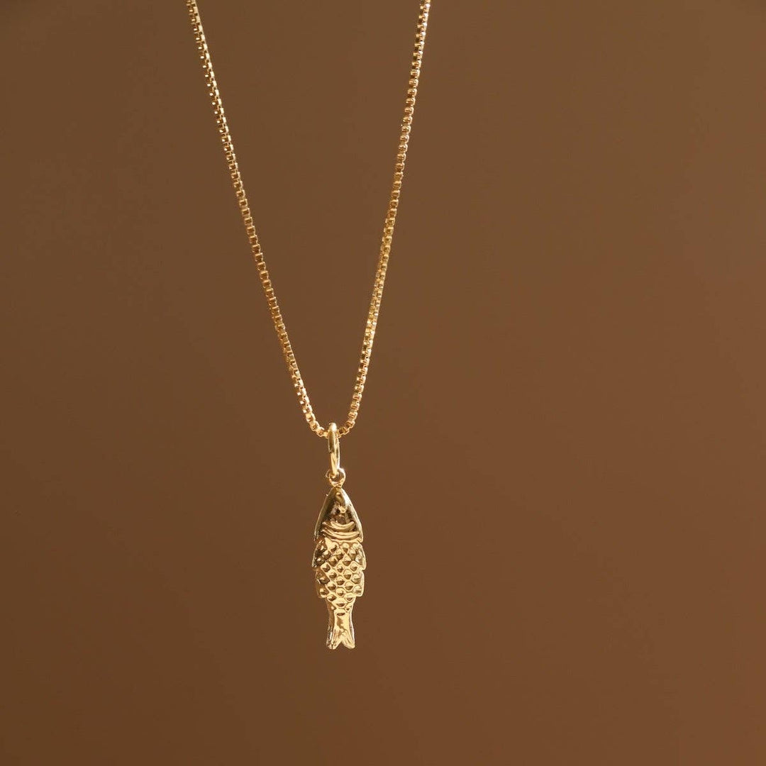 Gold fish-shaped pendant necklace on a beige background