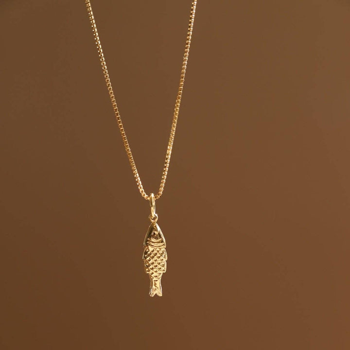 Gold fish-shaped pendant necklace on a beige background