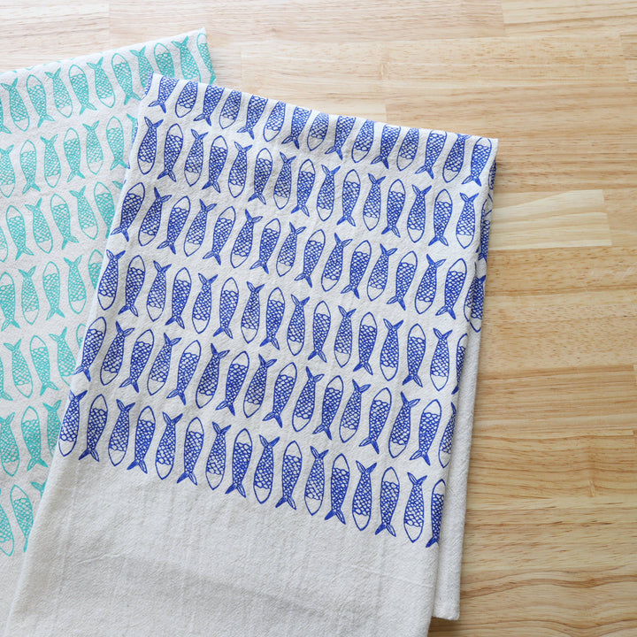 Two fabric towels with fish patterns on a wooden surface
