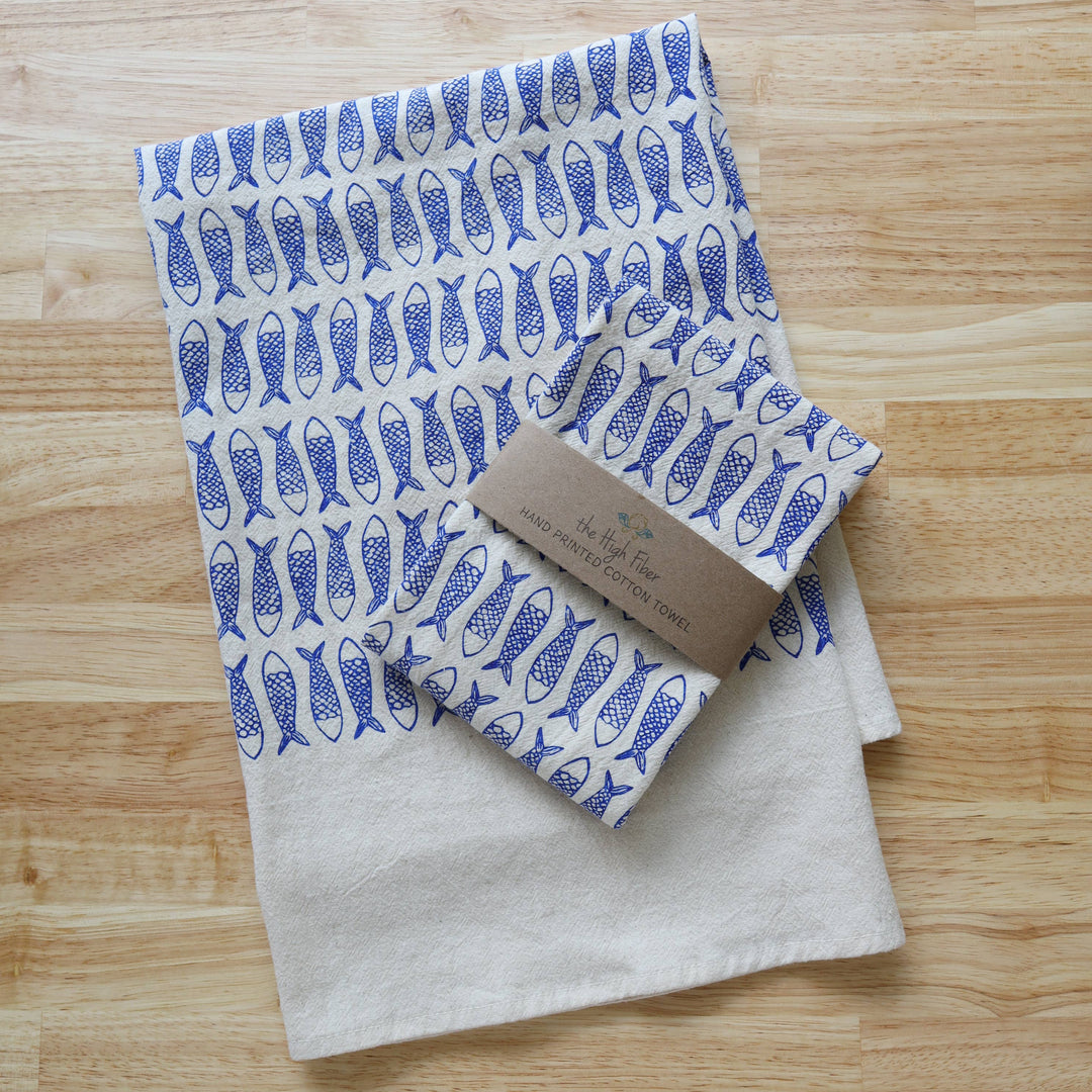 Two folded towels, one with a blue fish pattern and the other plain, on a wooden surface.