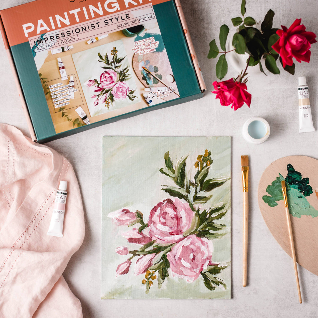 Floral painting kit with completed artwork, paintbrushes, and supplies on a light surface.