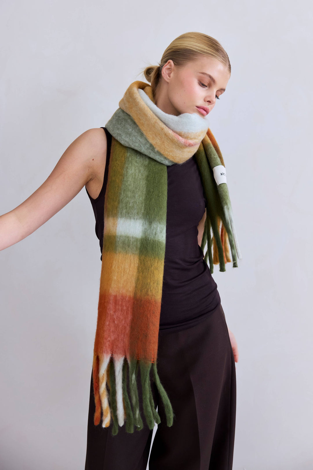 Woman wearing a fluffy green, orange and cream colored scarf with fringe.