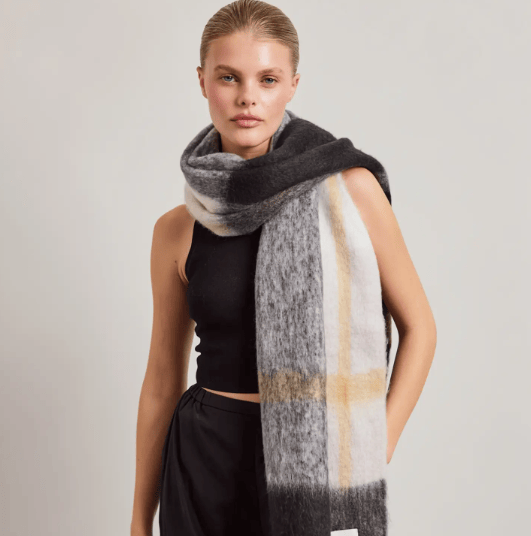 Woman wearing a cream, white and charcoal gray fluffy scarf.