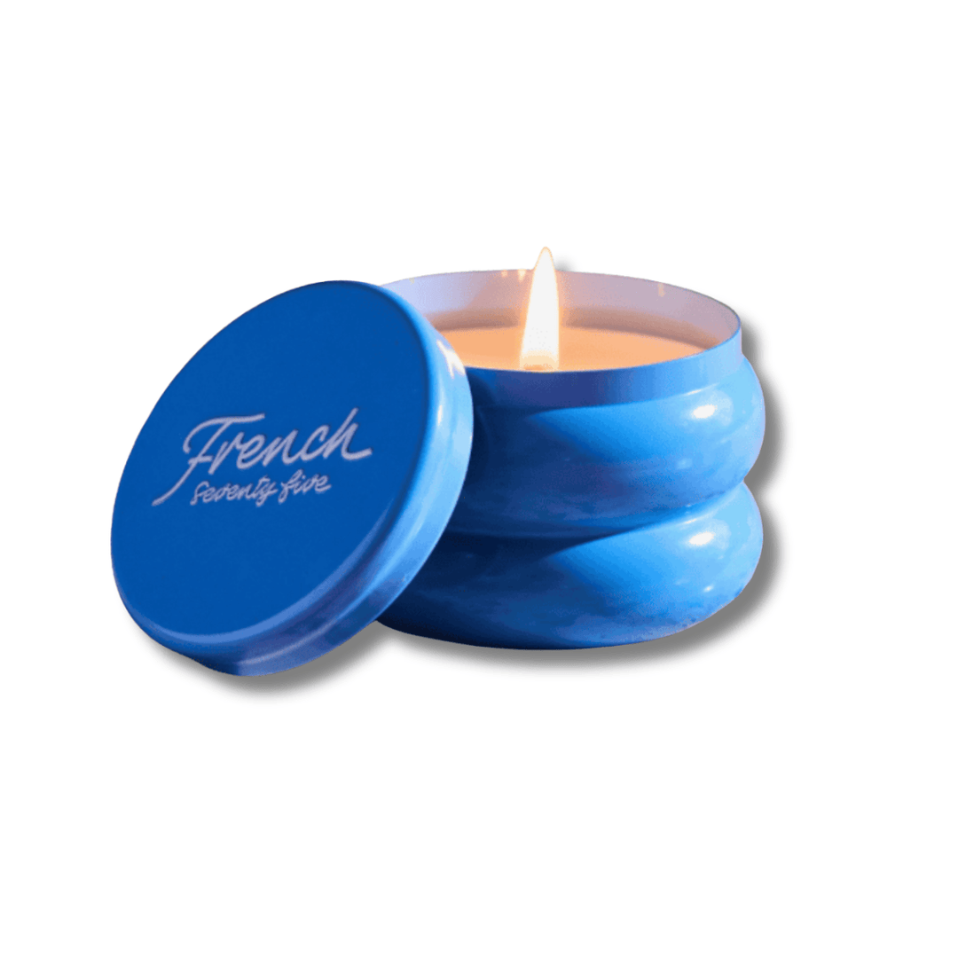 Blue French 75 candle in a tin with a lit wick on a white background