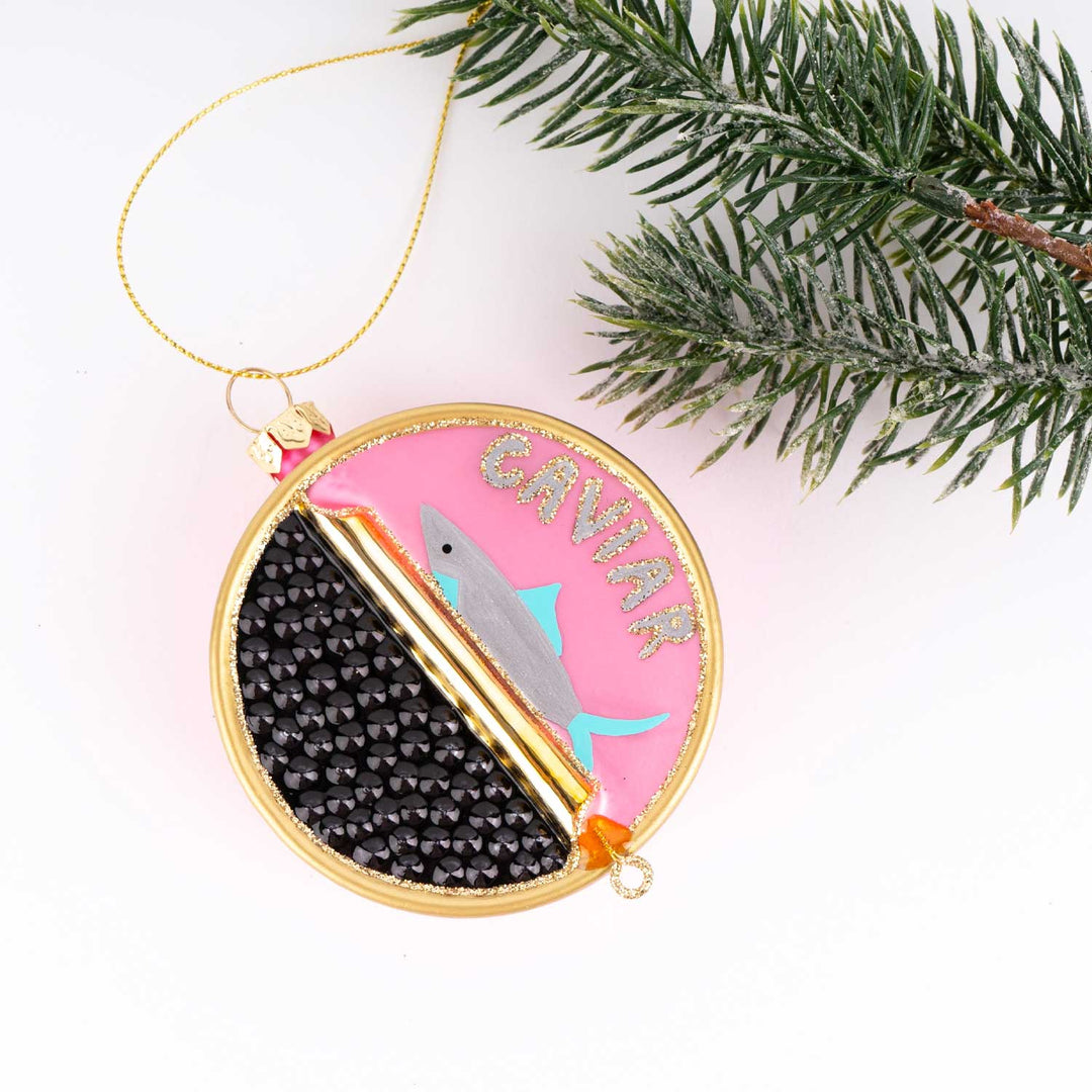 Decorative ornament with pink and black design, featuring the word 'Caviar', on a white background with a Christmas tree branch.