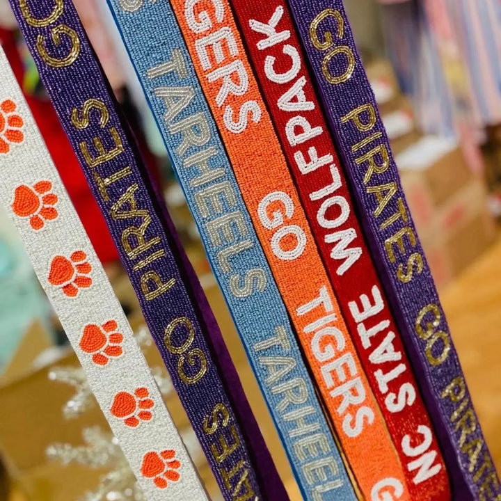 Collection of colorful bag straps with sports team names and paw prints.