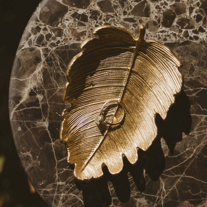 Gold leaf-shaped ring holder with a ring on a marble surface