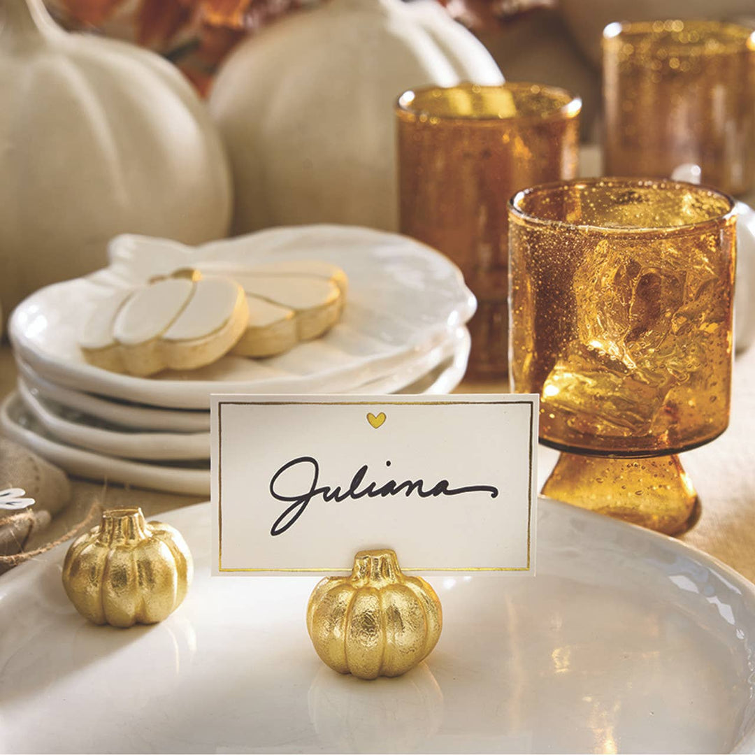 Table setting with gold pumpkin place card holder, white plates, and decorative glasses.