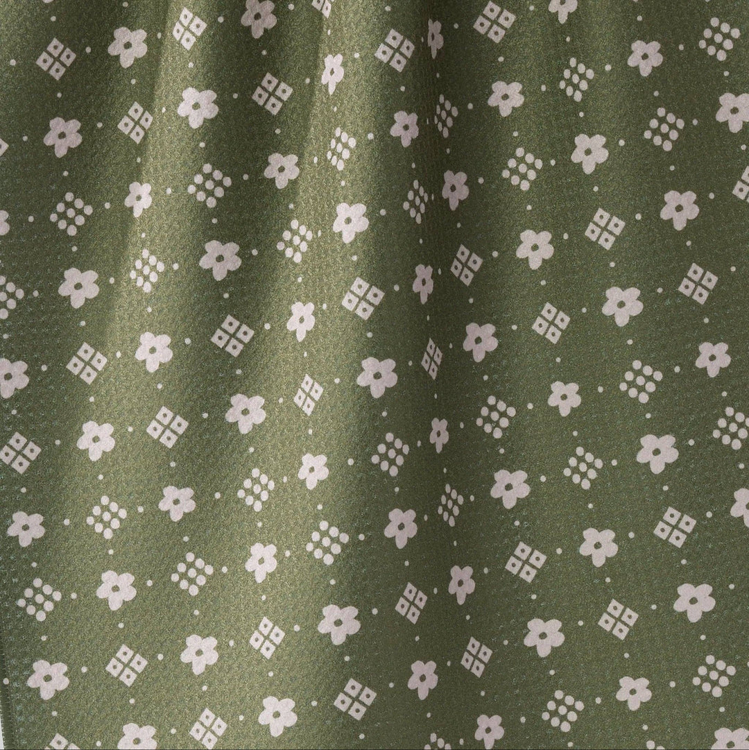 Close-up of olive green fabric with a repeating white floral and geometric pattern.