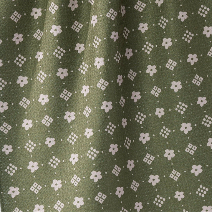 Close-up of olive green fabric with a repeating white floral and geometric pattern.
