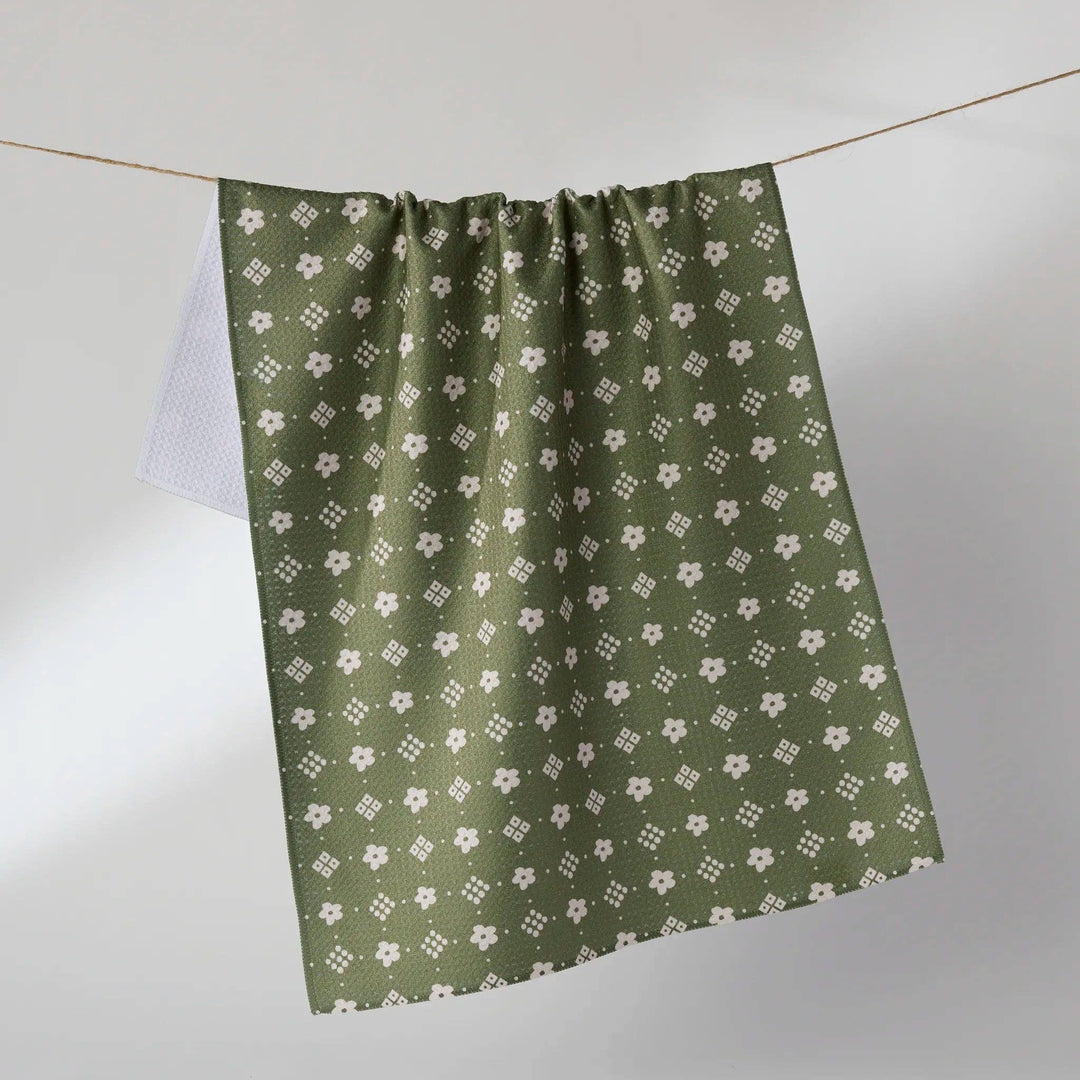 An olive green curtain panel with a repeating white floral and geometric pattern, hanging from a thin wire against a neutral gray background.